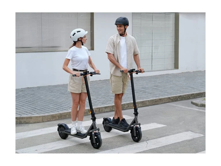 Two people in helmets with Xiaomi Electric Scooter 6 Lite scooters at a crosswalk